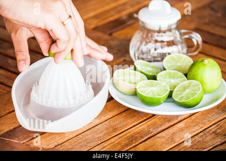 Schiacciamento delle mani di lime fresco sul contatore di legno Foto Stock