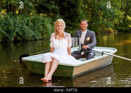 Bella giovane coppie in viaggio di nozze, bionda sposa con fiore e suo sposo appena sposati sulla piccola barca a stagno con sole serale Foto Stock