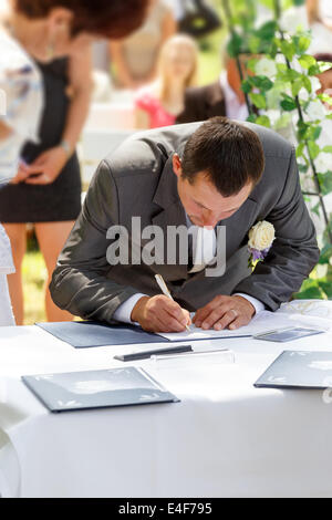 Lo sposo firma certificato di matrimonio nel parco con sposa in background Foto Stock