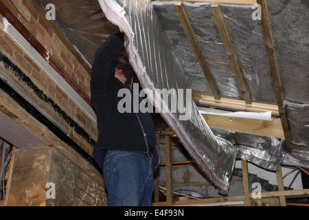 Workman installazione di isolamento di lamina in un spazio sul tetto. Foto Stock