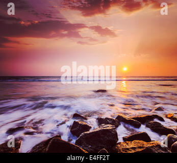 Vintage retrò hipster stile immagine di viaggio di tropical beach vacation background - le onde e le rocce sulla spiaggia sul tramonto Foto Stock