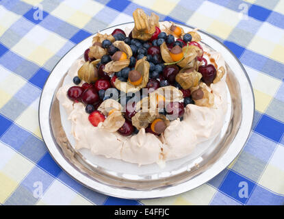 Frutta fresca Pavlova, meringue guarnita con frutta fresca inclusa physalis immersi nel cioccolato su un blu e tovaglia bianca Foto Stock