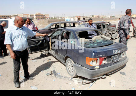 Kirkuk, Iraq. 10 Luglio, 2014. Persone ispezionare il sito di un attentato all'automobile intrappolata su vetture schierate in corrispondenza di una stazione di gas nella città di Kirkuk, nell Iraq del nord, 10 luglio 2014. L'attentato alla stazione di gas feriti sette persone qui il giovedì mattina. Credito: Dena Assad/Xinhua/Alamy Live News Foto Stock