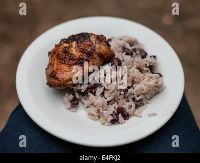 Una piastra di jerk coscia di pollo con riso e piselli bilanciato sulle ginocchia a un barbecue estivo. Foto Stock
