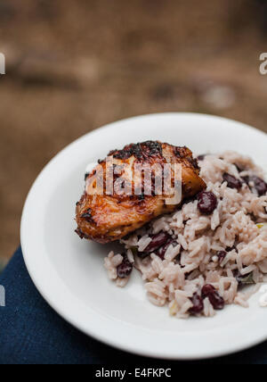 Una piastra di jerk coscia di pollo con riso e piselli bilanciato sulle ginocchia a un barbecue estivo. Foto Stock