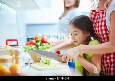 Ritratto di bambina aiutando la madre a cuocere in cucina Foto Stock