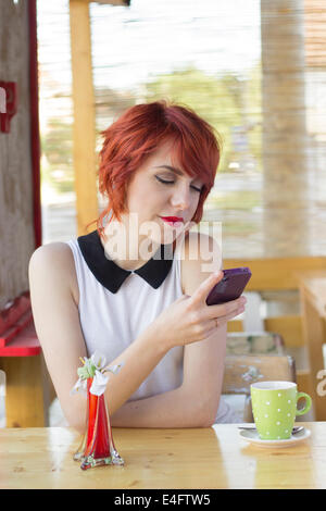 Carino hipster ragazza adolescente per la messaggistica di testo in un coffee shop Foto Stock