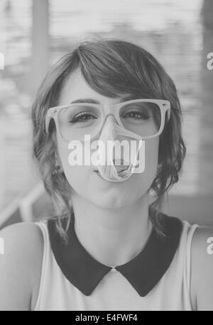 Carino hipster ragazza adolescente con grandi gomme da masticare bubble popping oltre il suo volto. In bianco e nero in stile retrò immagini Foto Stock