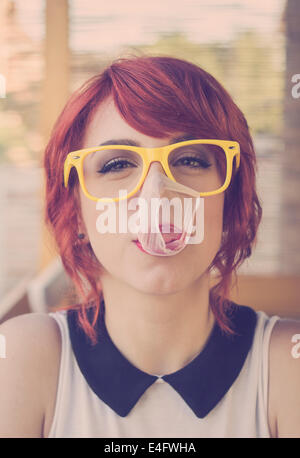 Carino hipster ragazza adolescente con grandi gomme da masticare bubble popping oltre il suo volto Foto Stock