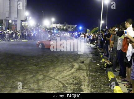 Tripoli. 11 Luglio, 2014. I libici guardare un giovane uomo deriva la sua auto in una strada di Tripoli Luglio 11, 2014. Dopo la rottura della veloce durante islamica del mese sacro del Ramadan, il popolo libico ha preso la strada per godere di estate fresca di notte. © Hamza Turkia/Xinhua/Alamy Live News Foto Stock