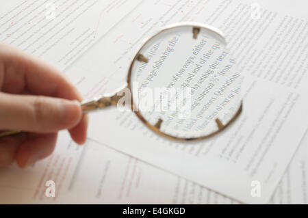 Vicino la mano che tiene la lente di ingrandimento per leggere il documento Foto Stock