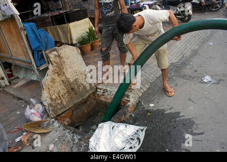 Gli uomini sono il pompaggio di acque luride da una gronda presa su una strada di città in Phnom Penh Cambogia. Foto Stock