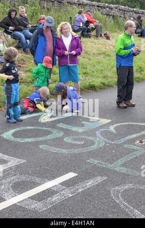 I bambini lo sfarinamento i nomi dei piloti su strada prima della data prevista di arrivo del Tour de France vicino Hawes, North Yorkshire, Inghilterra, Regno Unito Foto Stock