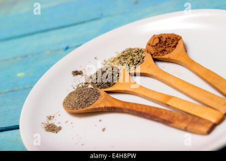 Insieme di diversi condimenti e spezie in piccoli cucchiai di legno disposte in scala su una piastra, primo piano Foto Stock