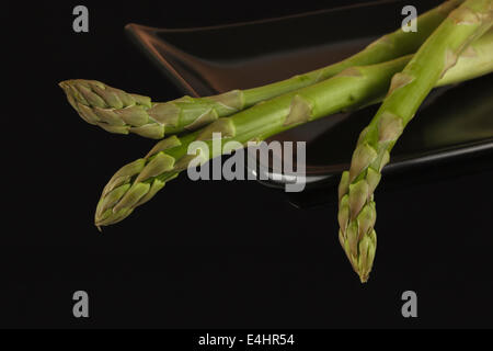 Tre di asparagi freschi sul piatto nero Foto Stock