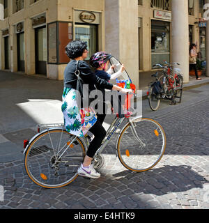 Donna (madre?) in sella a una moto con un giovane bambino seduto nel sedile tenendo parabrezza e indossando il casco a campana Foto Stock