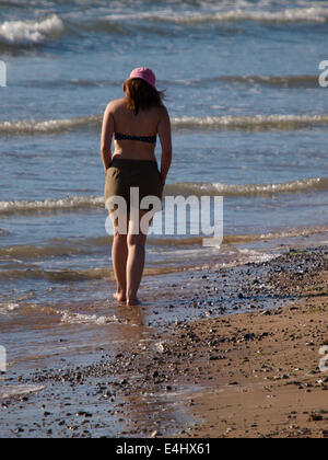 Giovane donna camminando lungo la riva del mare, Bude, Cornwall, Regno Unito Foto Stock