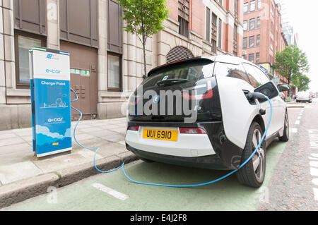 BMW i3 auto elettrico collegato a un pubblico stazione di carica in corrispondenza di una strada parcheggio bay. Foto Stock