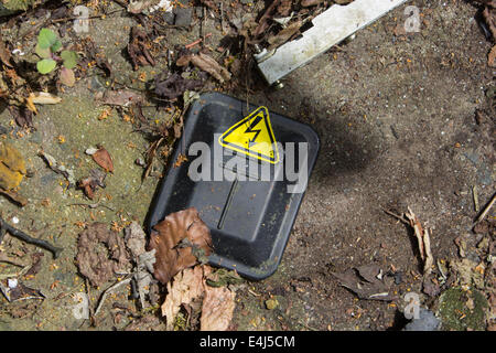 Immagine che mostra una sicurezza elettrica segno che è stato rotto e lasciato a terra tra la sporcizia Foto Stock