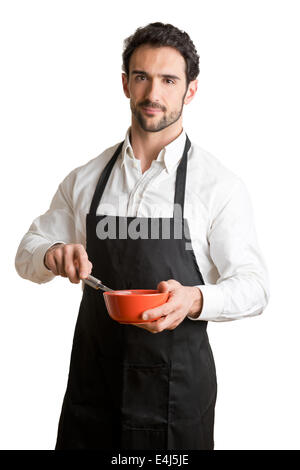 Fornello a maschio con un grembiule nero, sorridente e tenendo un uovo-battitore, isolato in bianco Foto Stock