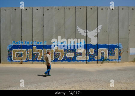 Un civile israeliano passa davanti a un muro prefabbricato di cemento decorato con mosaico comune che forma la scritta "Sentiero della pace" creata dai visitatori che scrivono un desiderio personale sul retro di un mosaico colorato e lo incollano al muro di difesa, adiacente alle case dell'insediamento israeliano Moshav Netiv HaAsara di fronte alla Striscia di Gaza settentrionale in Israele Foto Stock