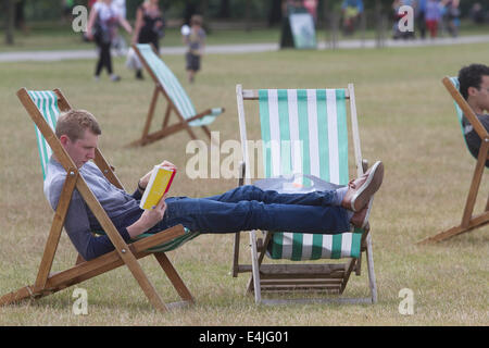 Kensington, London, Regno Unito. 13 Luglio, 2014. Un uomo che ama la lettura con i piedi sulle sedie a sdraio in Hyde Park Londra in una calda giornata di tempo soleggiato Credito: amer ghazzal/Alamy Live News Foto Stock