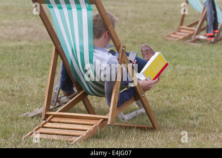 Kensington, London, Regno Unito. 13 Luglio, 2014. Un uomo che ama la lettura con i piedi sulle sedie a sdraio in Hyde Park Londra in una calda giornata di tempo soleggiato Credito: amer ghazzal/Alamy Live News Foto Stock