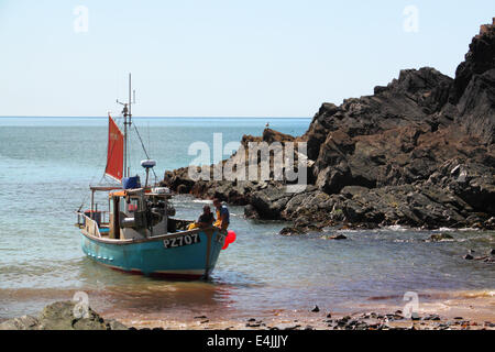 Un blu barca da pesca con un rosso di mezzana vela spiaggiata su un litorale roccioso. Foto Stock