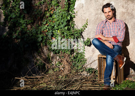 Sorridente modello maschile seduto sulla cassa di legno con le gambe incrociate Foto Stock