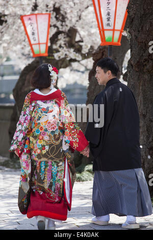 Coppia giovane nei tradizionali abiti da cerimonia a piedi lungo Shusei no Michi in Higashi Chaya, Kanazawa tra ciliegi fioriti Foto Stock