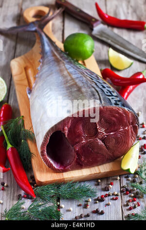 Crudo fresco di coda di tonno su tavola di legno con red hot chili pepper, lime fresco e aneto. Messa a fuoco selettiva. Foto Stock