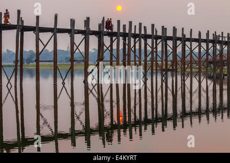 I monaci passeggiata attraverso la U Bein ponte in teak al tramonto. Il ponte si estende per 1200 metri lungo il lago Taungthaman in Myanmar. Foto Stock