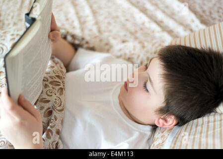 Ragazzo la lettura di un libro prima di andare a dormire sdraiati a letto Foto Stock