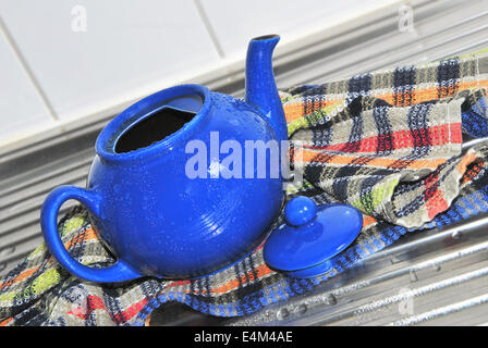 Blue tè pentola con acqua scende in un colorato a scacchi asciugamano da cucina sul lavello da cucina, close up Foto Stock