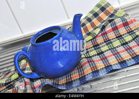 Blue tè pentola con acqua scende in un colorato a scacchi asciugamano da cucina sul lavello da cucina, close up Foto Stock