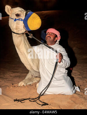 Uomo beduino nel tradizionale abito arabo pone con il suo cammello in un safari nel deserto camp fuori Dubai, UAE, dove i visitatori possono di Foto Stock