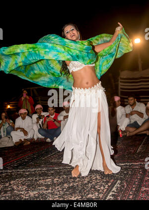 Una danzatrice del ventre ghirigori per gli ospiti a beduino desert safari camp fuori Dubai, UAE, dove i visitatori possono godere di una corsa in cammello, provare Foto Stock