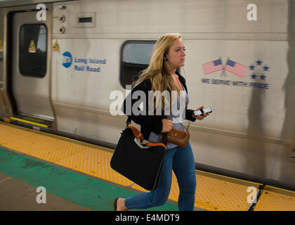 Merrick, New York, Stati Uniti - 14 Luglio 2014 - in serata durante le ore di punta, giovane donna che ha avuto il treno indossa telefono cellulare auricolari come lei corre sulla piattaforma sopraelevata di Merrick stazione ferroviaria di Babilonia il ramo, dopo MTA Metropolitan Transit Authority e Long Island Rail Road unione parla deadlock, con potenziale sciopero LIRR aleggiano pochi giorni prima. Credito: Ann e Parry/Alamy Live News Foto Stock