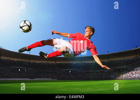 Giocatore di calcio calciare il pallone in Mid-Air Foto Stock