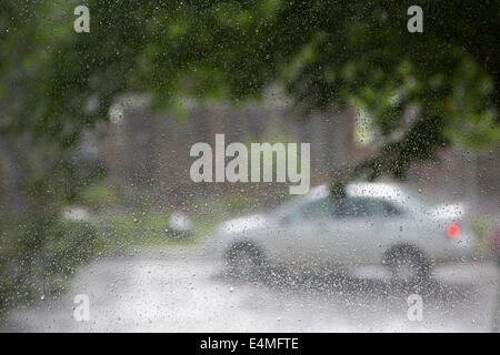 Auto sulla strada della città durante una giornata di pioggia visto attraverso gocce di pioggia sulla finestra di casa Foto Stock