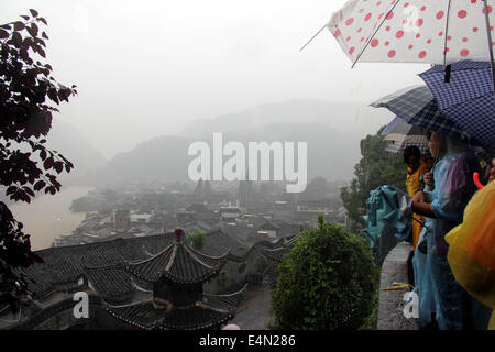 Xiangxi, Cina. Il 15 luglio 2014. I turisti riparo dalla pioggia nella contea di Fenghuang di centrale cinese di Hunan ProvinceMore a 120.000 residenti e turisti sono stati evacuati da lunedì notte come registrare gli acquazzoni hit Fenghuang County, una destinazione turistica rinomata per la sua antica città. Alimentazione nella contea è stata tagliata e diversi insediamenti temporanei istituito nella contea sedile per ospitare le persone evacuate. Il locale ufficio idrografico ha emesso un allarme rosso, il livello più alto nel paese del quattro-tier sistema di avvertimento, alle 10:10 a.m. martedì. Credito: Xinhua/Alamy Live News Foto Stock
