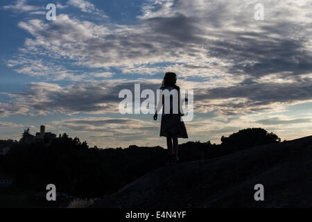 Silhouette di donna perso al tramonto in un abito tenendo un sacchetto con le nuvole in background Foto Stock