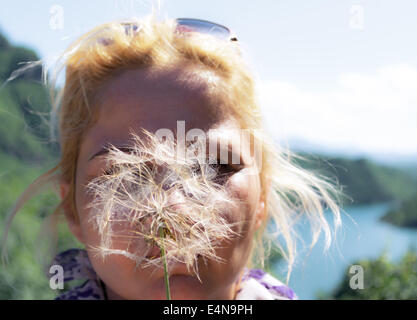 Una donna bionda che soffia su un dente di leone di esprimere un desiderio Foto Stock