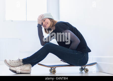 Giovane donna seduta su skateboard Foto Stock