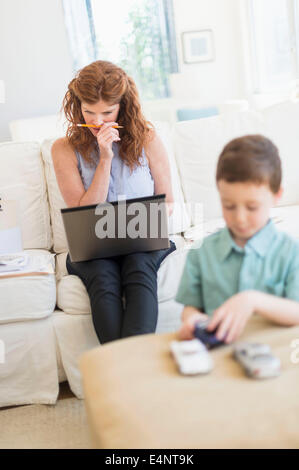 Madre utilizzando laptop, figlio (6-7) giocando con automobili giocattolo Foto Stock