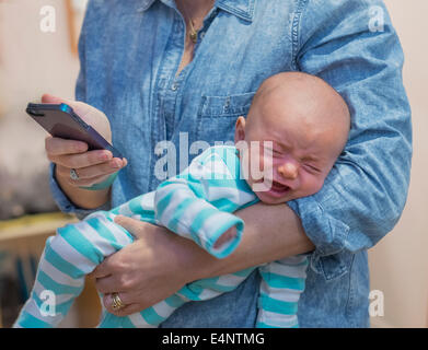 Donna sms e tenendo il pianto baby boy (2-5 mesi) Foto Stock