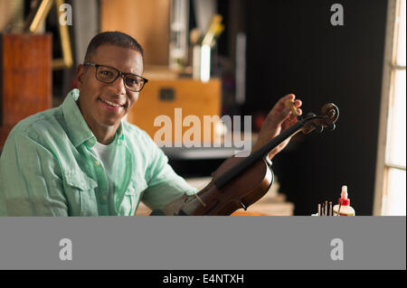 Ritratto di uomo maturo che fissa il violino nel suo laboratorio Foto Stock