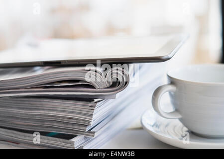 Ravvicinata di una tazza di caffè e tavoletta digitale sulla parte superiore della pila di magazzino Foto Stock