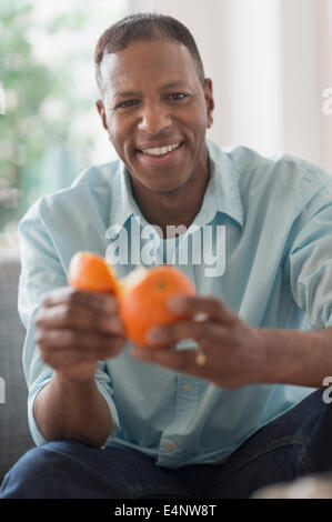 Ritratto di uomo sorridente sbucciare la frutta di arancia Foto Stock