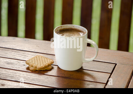 Tazza fumante di caffè caldo in tazza bianca e cookie biscotto sulla tavola in outdoor bower. Foto Stock